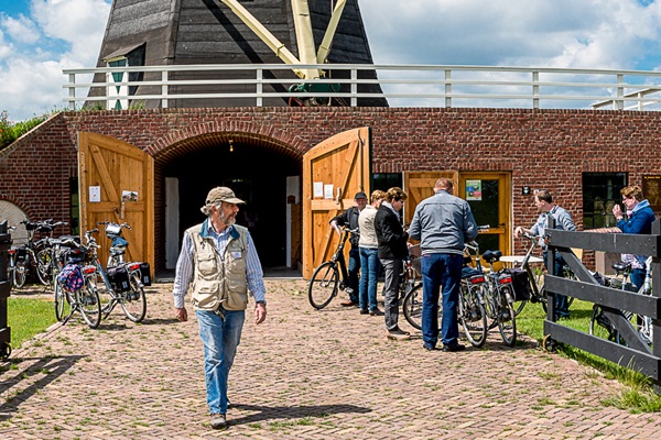 Man walks away from a mill as cyclists dismount to view the mill
